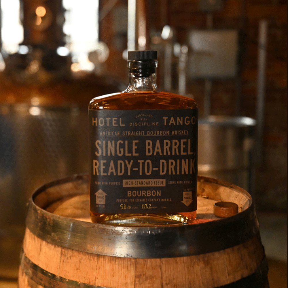 Cask Strength Single Barrel 63 bottle resting on top of a cask, with a still in the background.